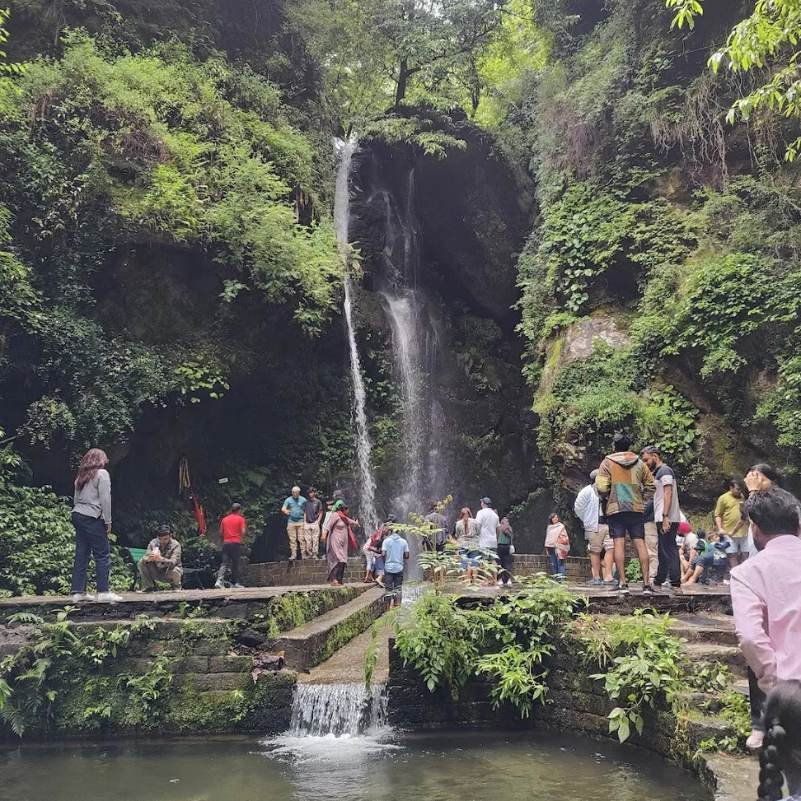 A misty morning at Jibhi Waterfall in the Banjar valley of Kullu district, Himachal Pradesh, with a modest cascade falling over a forested rock wall