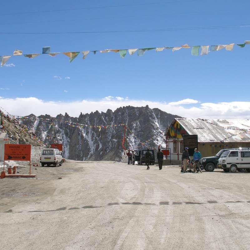 Buddhist prayer flags strung across the summit of Khardung La pass in strong wind, one of the signature images of the crossing